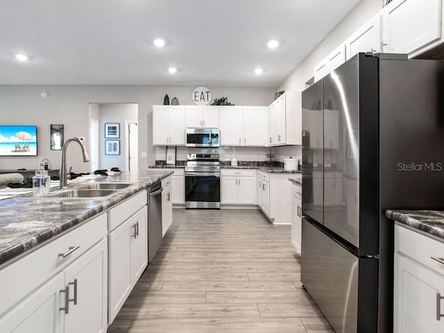 kitchen with sink, stainless steel appliances, dark stone counters, white cabinets, and light hardwood / wood-style flooring