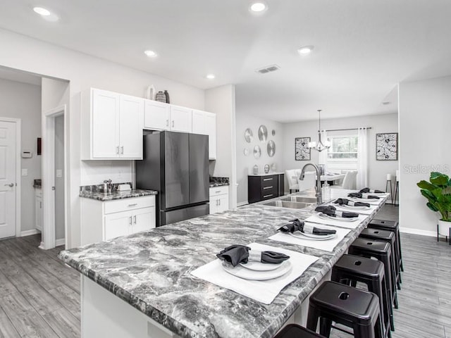 kitchen featuring white cabinets, light hardwood / wood-style floors, sink, and stainless steel fridge