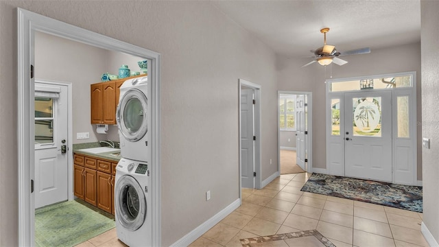 clothes washing area with cabinets, a textured ceiling, sink, stacked washer / dryer, and light tile patterned floors