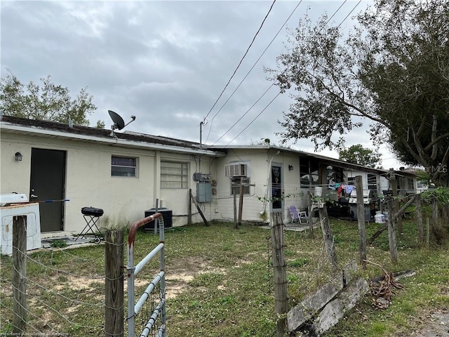 rear view of property featuring central air condition unit, a lawn, and a wall mounted air conditioner