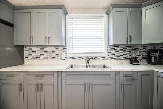 kitchen with sink, decorative backsplash, gray cabinetry, and a textured ceiling