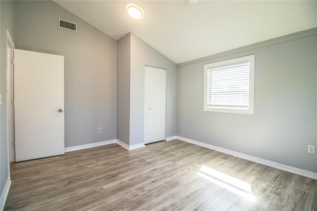 unfurnished bedroom with a closet, a textured ceiling, vaulted ceiling, and light wood-type flooring