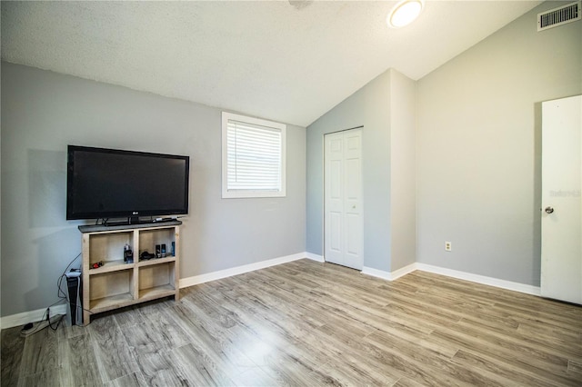 bedroom with vaulted ceiling, light hardwood / wood-style flooring, a textured ceiling, and a closet