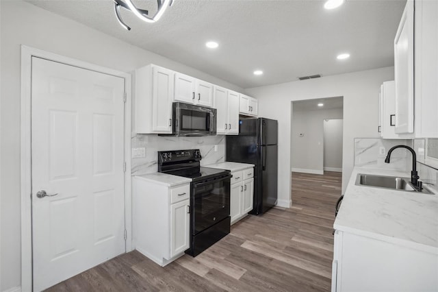 kitchen featuring tasteful backsplash, white cabinetry, black appliances, light hardwood / wood-style floors, and sink