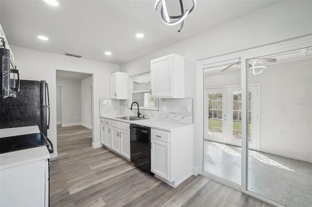 kitchen with black dishwasher, sink, light wood-type flooring, white cabinets, and a textured ceiling