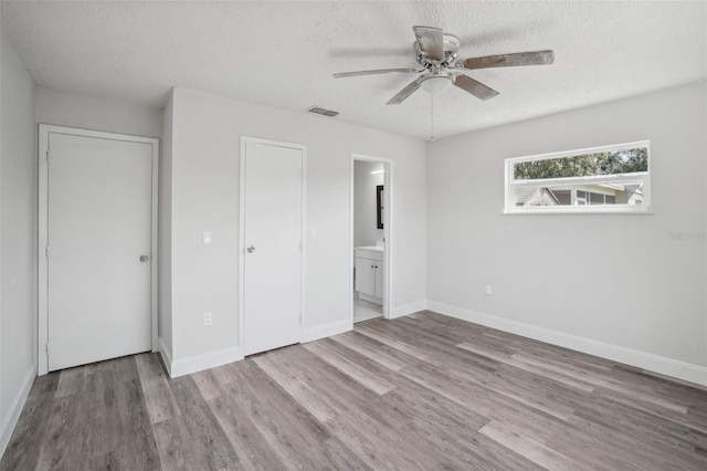 unfurnished bedroom featuring a textured ceiling, ensuite bath, light wood-type flooring, and ceiling fan