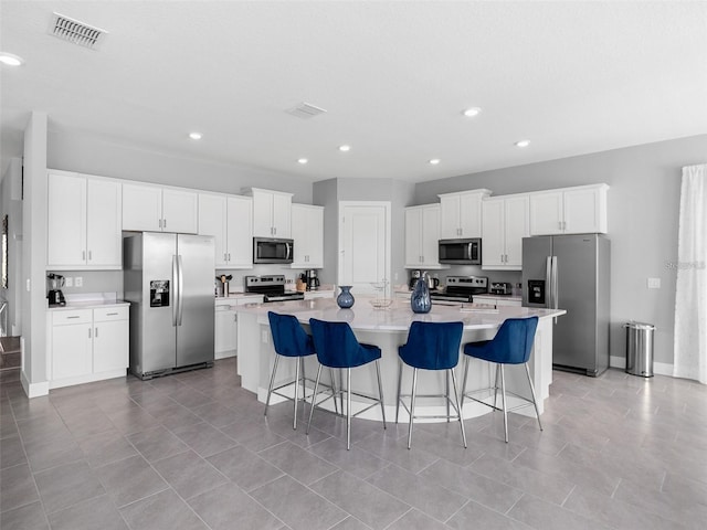 kitchen featuring a spacious island, a breakfast bar area, stainless steel appliances, light tile patterned floors, and white cabinets