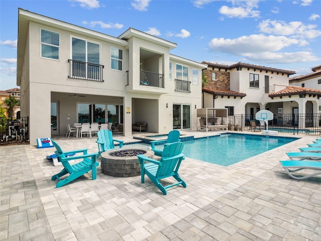 back of property with a balcony, an outdoor fire pit, a patio area, and a fenced in pool