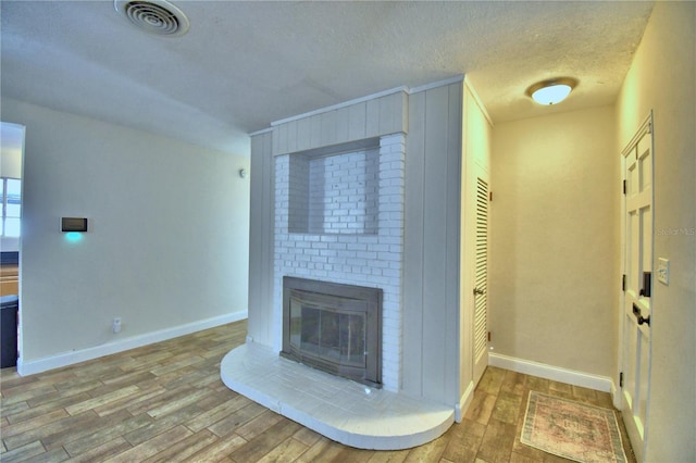 unfurnished living room with a brick fireplace, hardwood / wood-style floors, and a textured ceiling