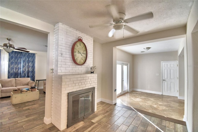 unfurnished living room featuring a brick fireplace, french doors, a textured ceiling, and ceiling fan