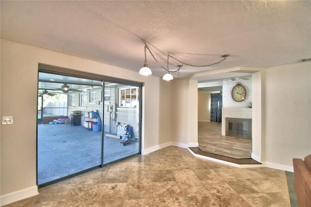 unfurnished room featuring a brick fireplace, plenty of natural light, a textured ceiling, and ceiling fan