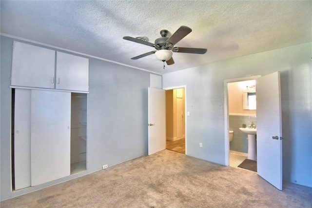 unfurnished bedroom featuring ensuite bath, light colored carpet, a textured ceiling, a closet, and ceiling fan