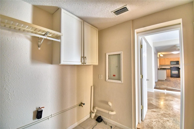 laundry area featuring cabinets, electric panel, and a textured ceiling