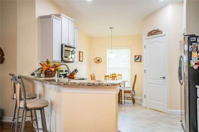 kitchen featuring stone counters, appliances with stainless steel finishes, a kitchen bar, hanging light fixtures, and white cabinetry