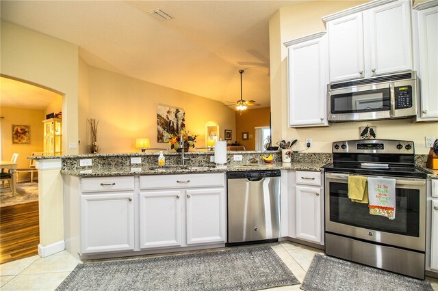 kitchen with kitchen peninsula, dark stone countertops, white cabinets, appliances with stainless steel finishes, and ceiling fan