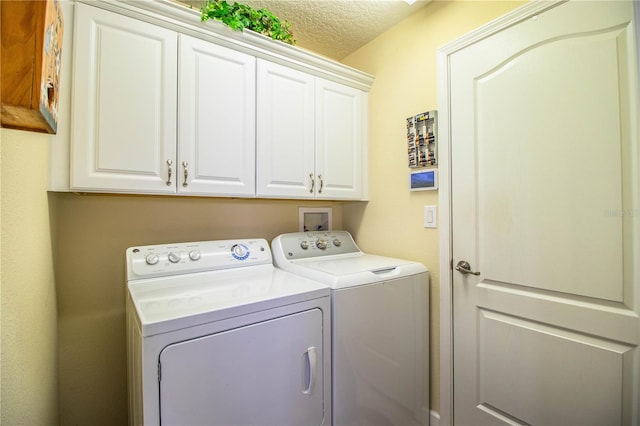 laundry area with washing machine and clothes dryer, a textured ceiling, and cabinets