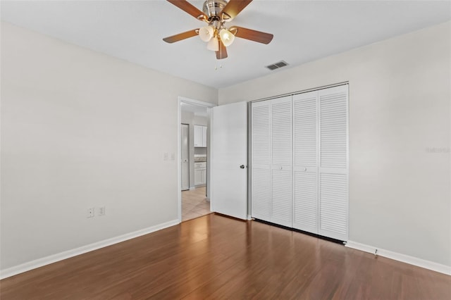 unfurnished bedroom featuring visible vents, ceiling fan, a closet, baseboards, and wood finished floors