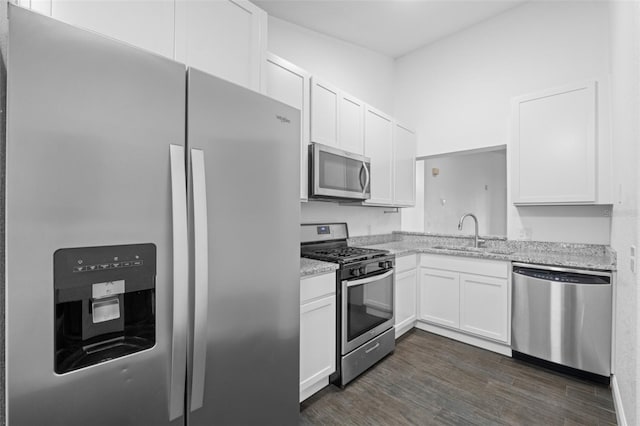 kitchen with appliances with stainless steel finishes, dark hardwood / wood-style floors, light stone counters, and white cabinetry