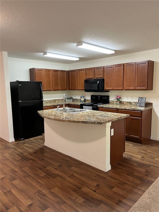 kitchen with a kitchen island with sink, dark wood-type flooring, sink, black appliances, and a textured ceiling