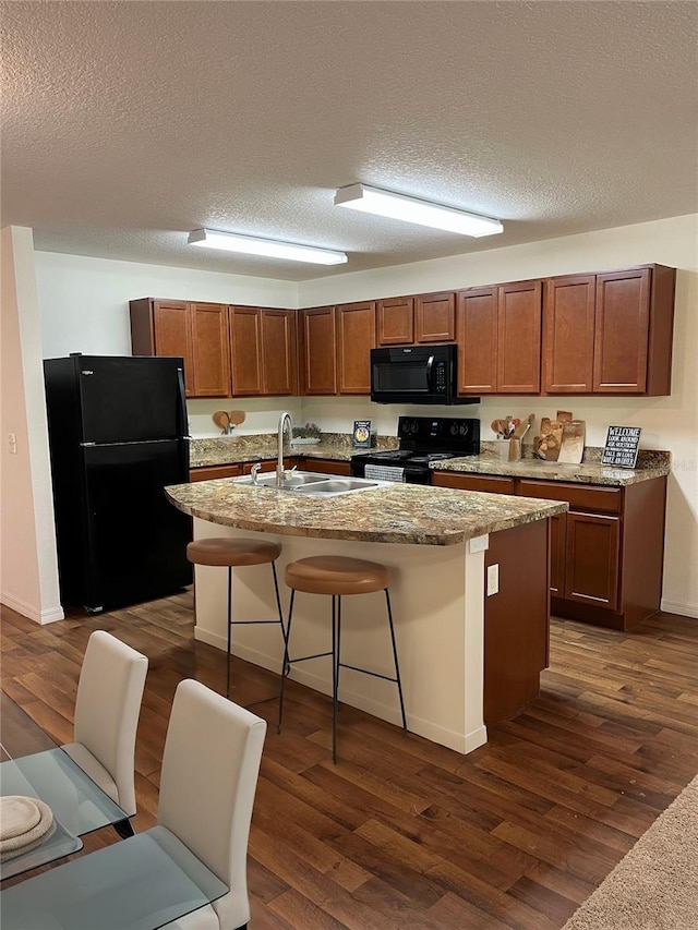 kitchen with black appliances, sink, a textured ceiling, a kitchen breakfast bar, and a kitchen island with sink