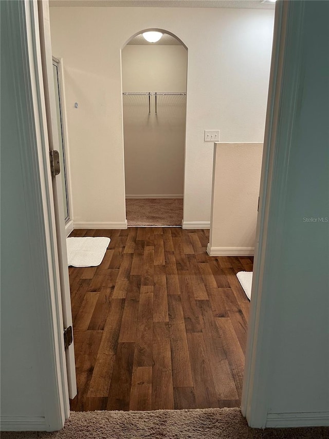 hallway with arched walkways, dark wood-style floors, and baseboards