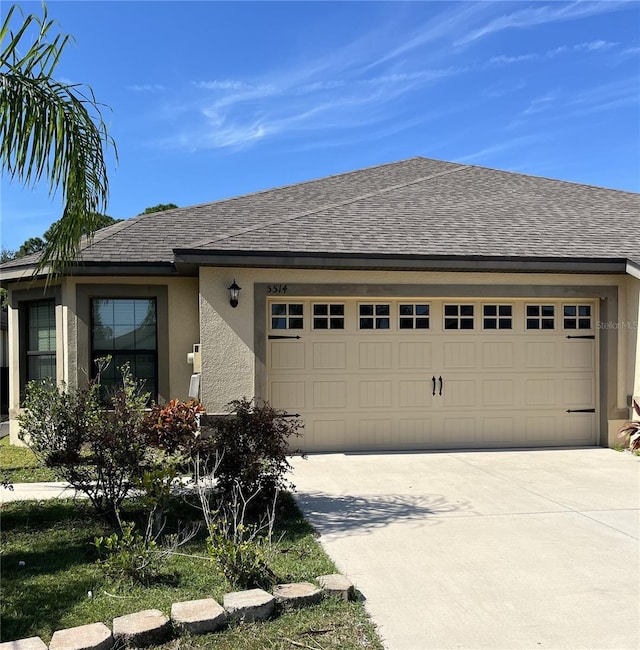 view of front facade featuring an attached garage, a shingled roof, concrete driveway, and stucco siding