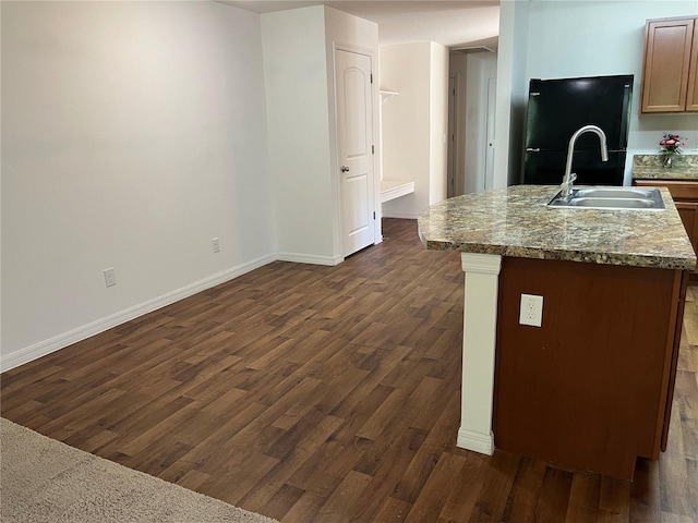 kitchen with a kitchen island with sink, a sink, baseboards, freestanding refrigerator, and dark wood finished floors