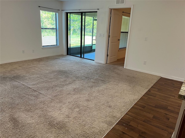 empty room with dark wood-type flooring, visible vents, dark carpet, and baseboards