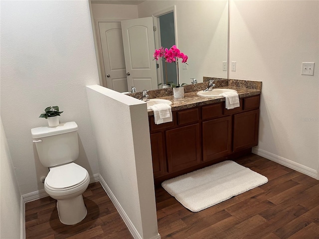 full bathroom with toilet, a sink, wood finished floors, baseboards, and double vanity