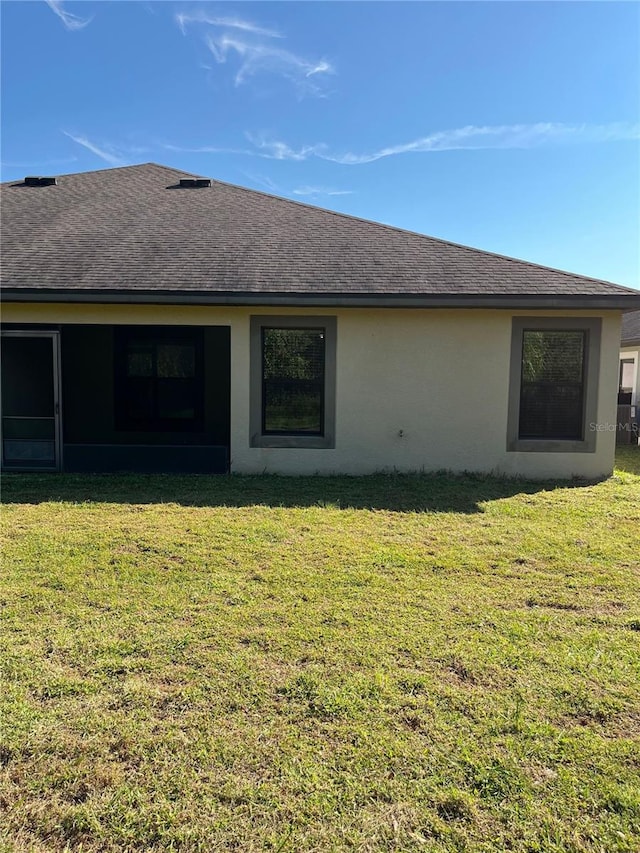 back of property with roof with shingles, a yard, and stucco siding