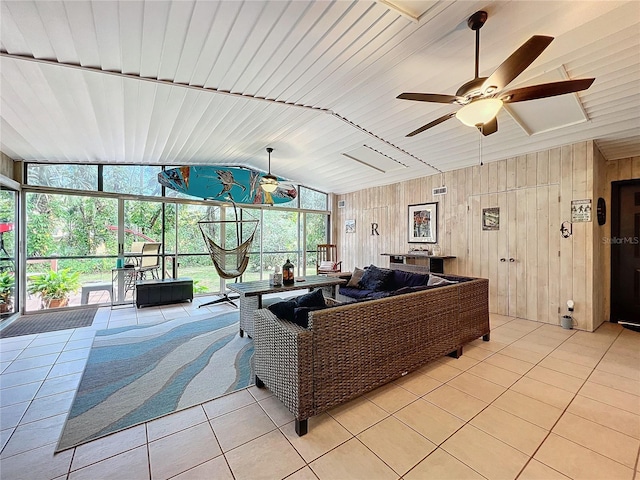 living room with lofted ceiling, wooden walls, light tile patterned floors, and ceiling fan