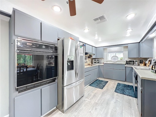 kitchen with stainless steel appliances, sink, light wood-type flooring, gray cabinets, and ceiling fan