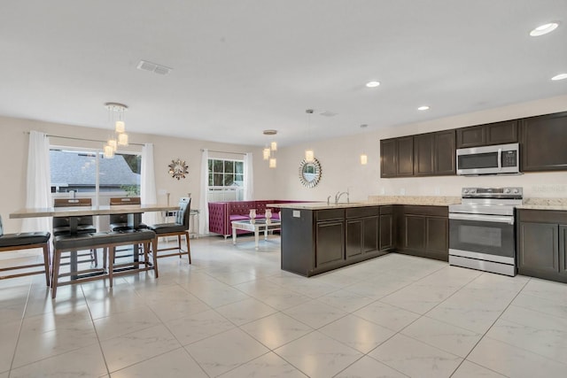 kitchen with kitchen peninsula, stainless steel appliances, sink, dark brown cabinetry, and decorative light fixtures