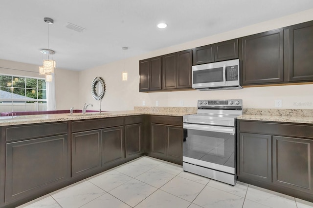 kitchen with light stone countertops, sink, dark brown cabinets, stainless steel appliances, and pendant lighting