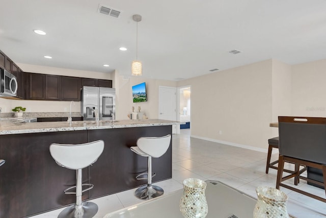 kitchen with light tile patterned floors, a breakfast bar, light stone countertops, pendant lighting, and stainless steel appliances