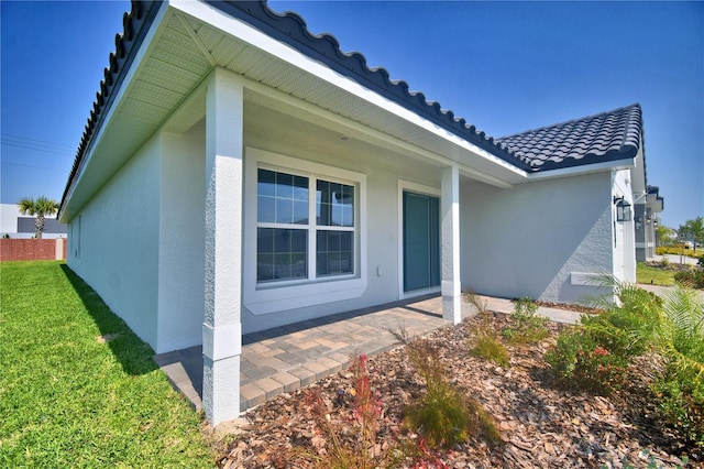 doorway to property featuring stucco siding, a tiled roof, and a yard
