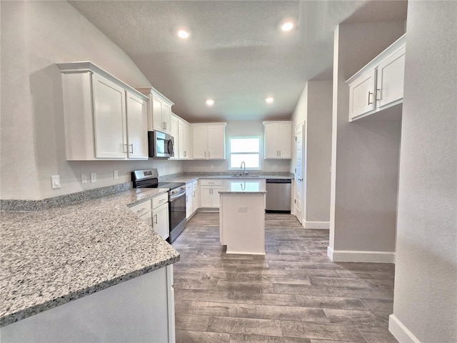 kitchen featuring white cabinets, wood finished floors, stainless steel appliances, a sink, and light stone counters