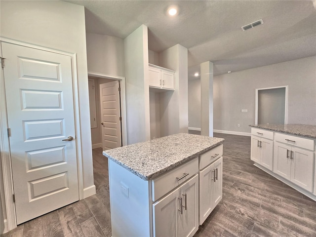 kitchen featuring white cabinets, a center island, dark wood-style floors, and visible vents