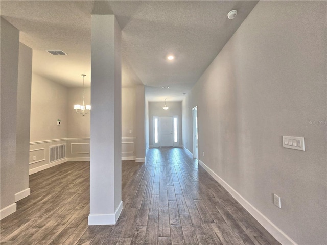 corridor with dark wood-style flooring, a textured ceiling, and visible vents