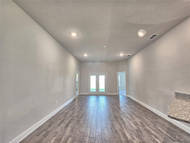 unfurnished living room with dark wood finished floors, a textured ceiling, baseboards, and visible vents