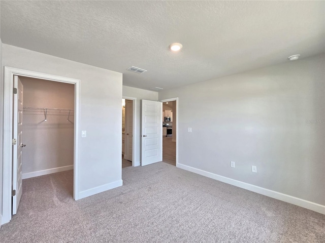 unfurnished bedroom featuring a walk in closet, carpet, baseboards, and a textured ceiling