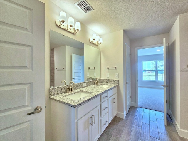 bathroom with double vanity, a sink, a textured ceiling, and visible vents