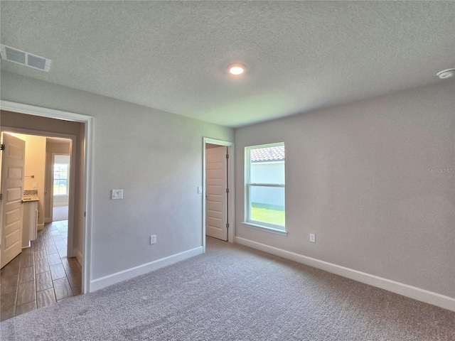 unfurnished bedroom featuring carpet, baseboards, a textured ceiling, and visible vents