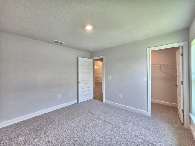 unfurnished bedroom with carpet flooring, a spacious closet, a textured ceiling, baseboards, and visible vents