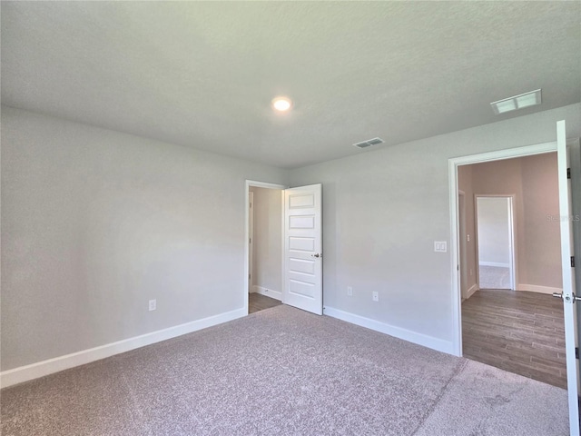 unfurnished bedroom featuring baseboards, dark carpet, and visible vents
