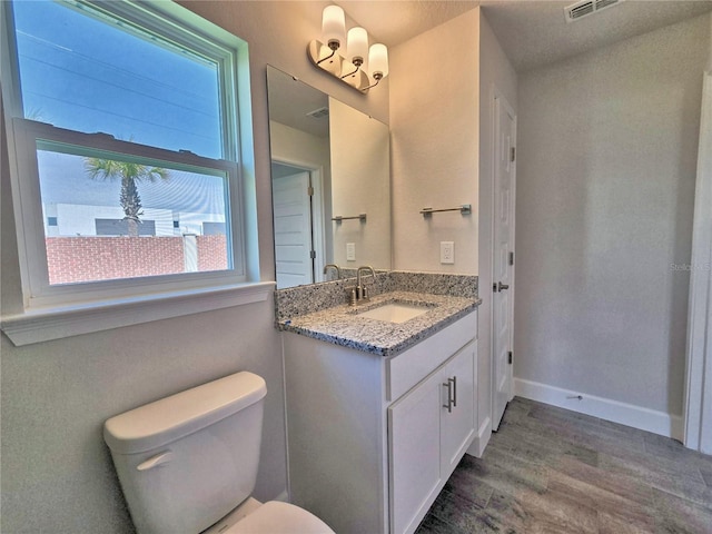 bathroom featuring visible vents, baseboards, toilet, wood finished floors, and vanity