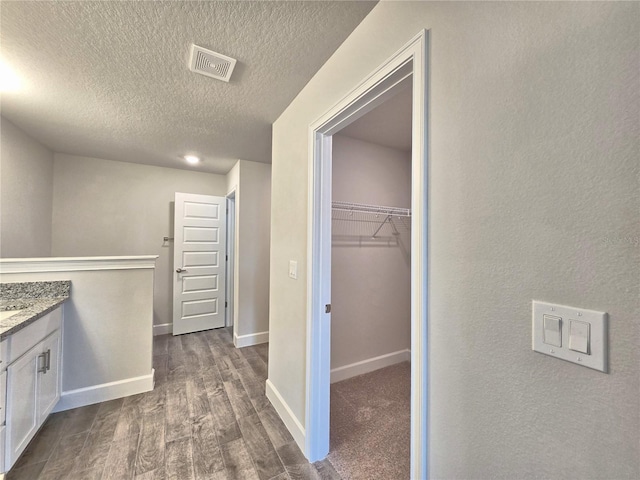 hall with baseboards, a textured ceiling, visible vents, and dark wood finished floors