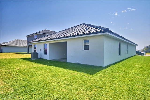 back of house featuring cooling unit, a tile roof, stucco siding, and a lawn