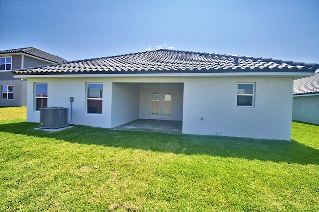 rear view of property featuring cooling unit, stucco siding, french doors, and a lawn