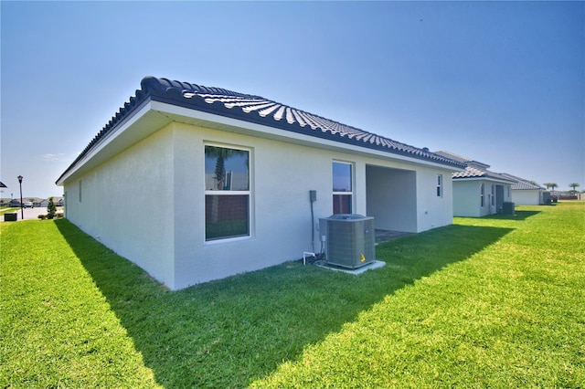 rear view of property featuring cooling unit, a tiled roof, stucco siding, and a lawn